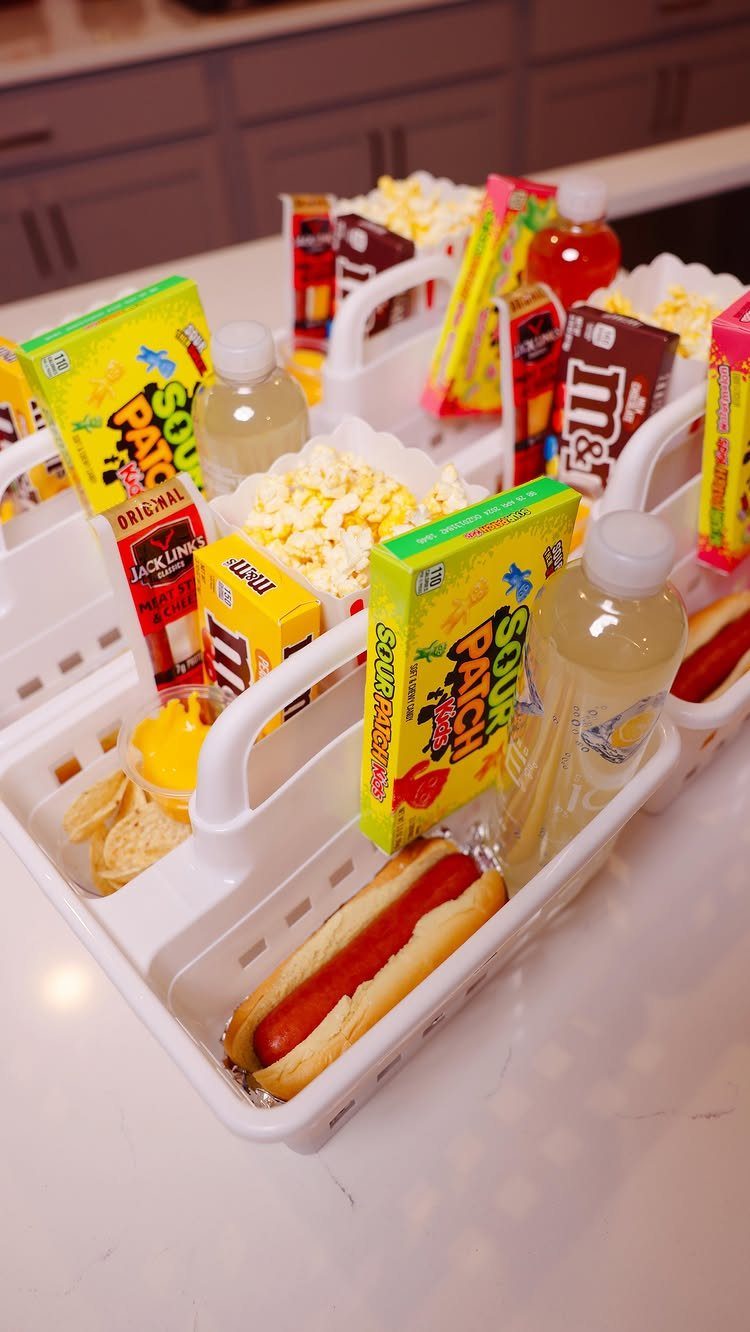 White baskets filled with popcorn, candy, bottled water, and hot dogs for movie night.