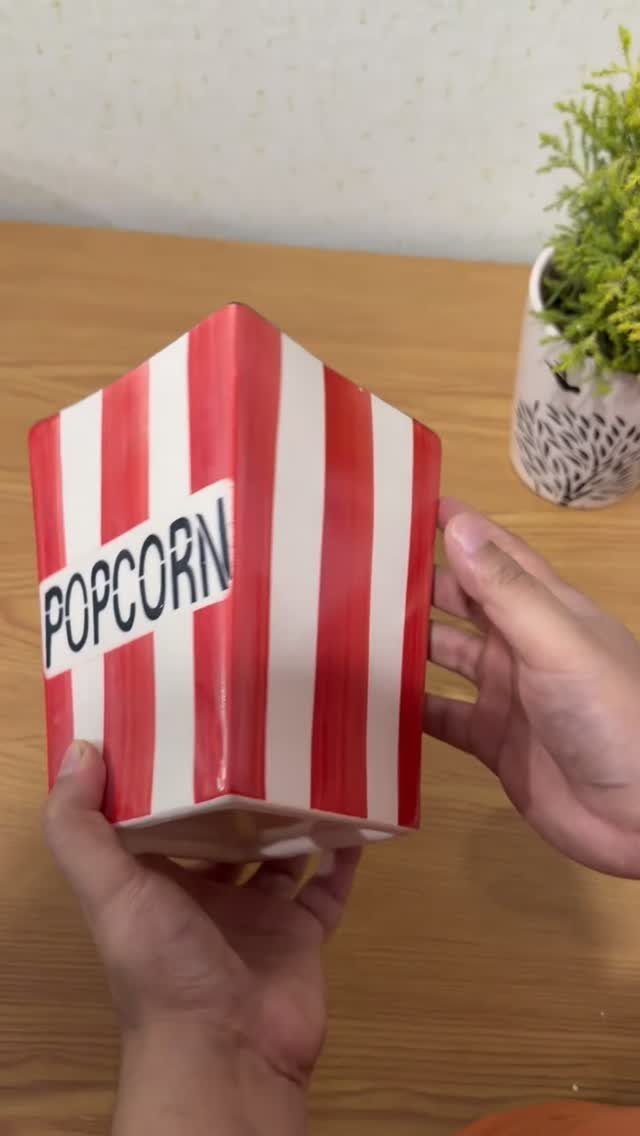 Red and white striped ceramic popcorn bucket held by two hands on wooden table