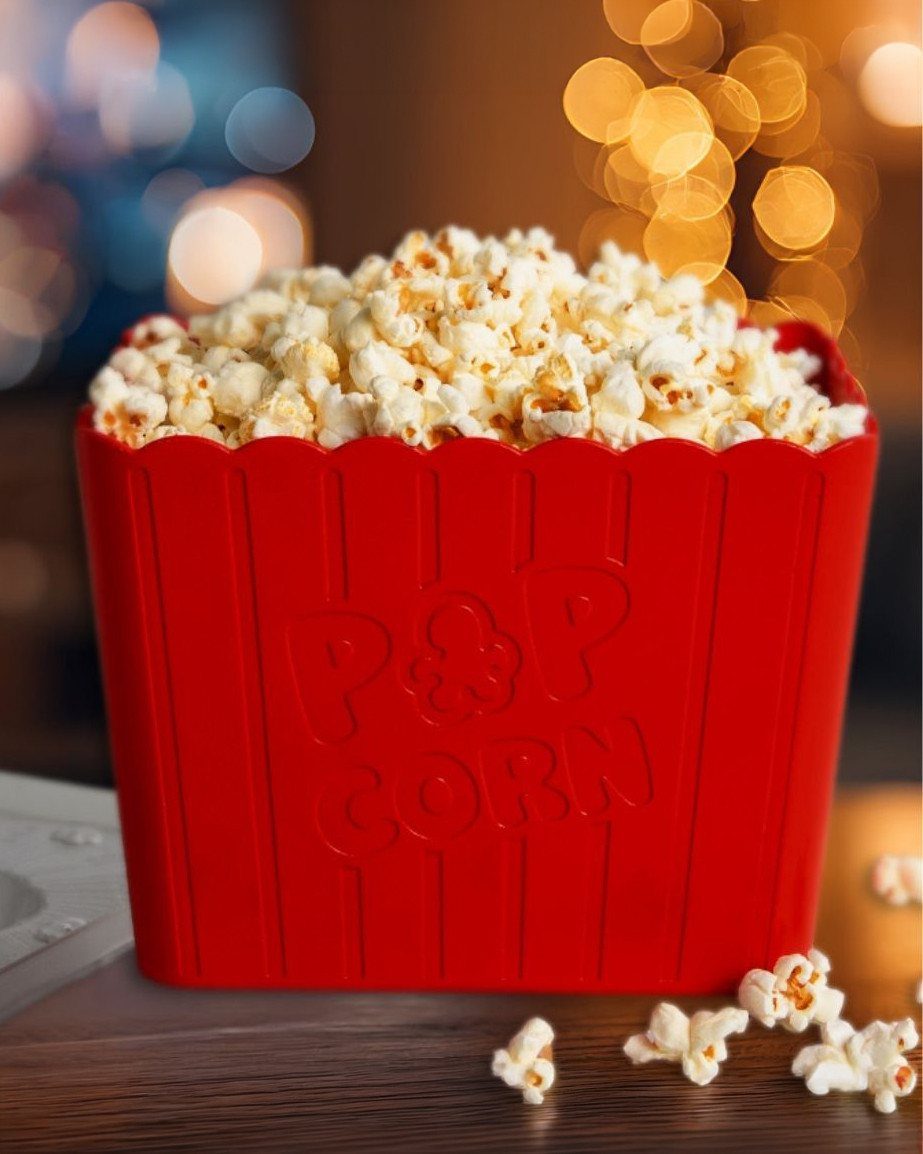 Red popcorn bucket filled with popped corn on a wooden table with bokeh lights.