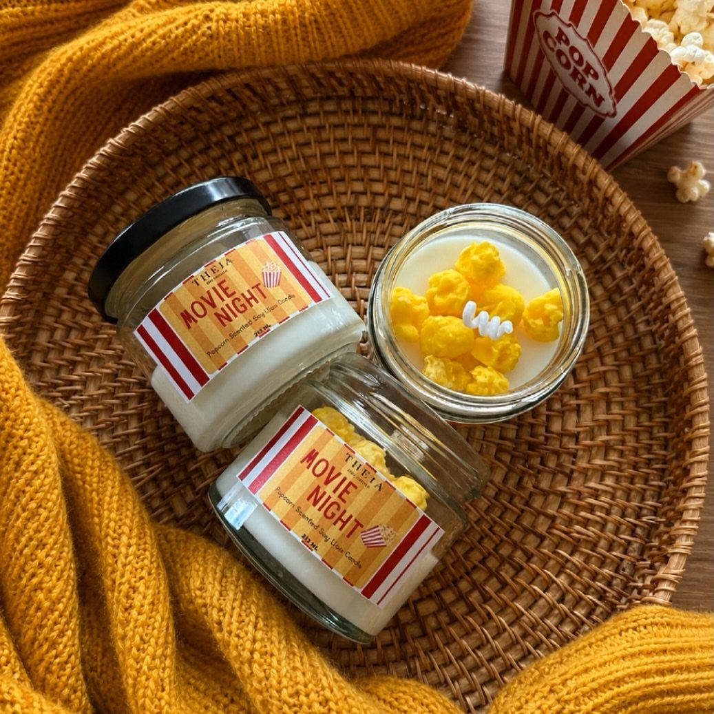 Movie night scented candles in glass jars on a woven tray with popcorn.