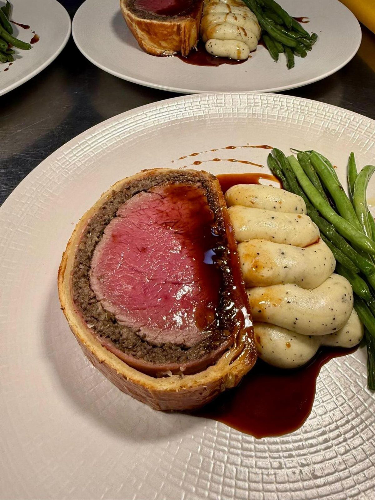 Beef Wellington slice with mashed potatoes and green beans on a white plate.