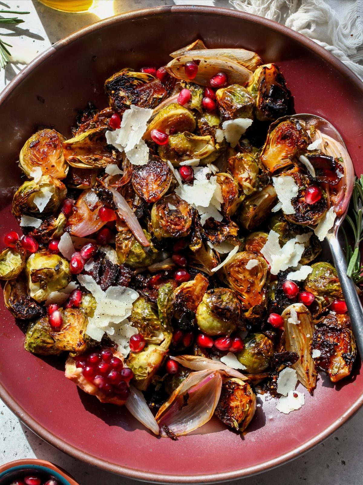 Roasted Brussels sprouts with pomegranate seeds and shaved cheese in a red bowl.