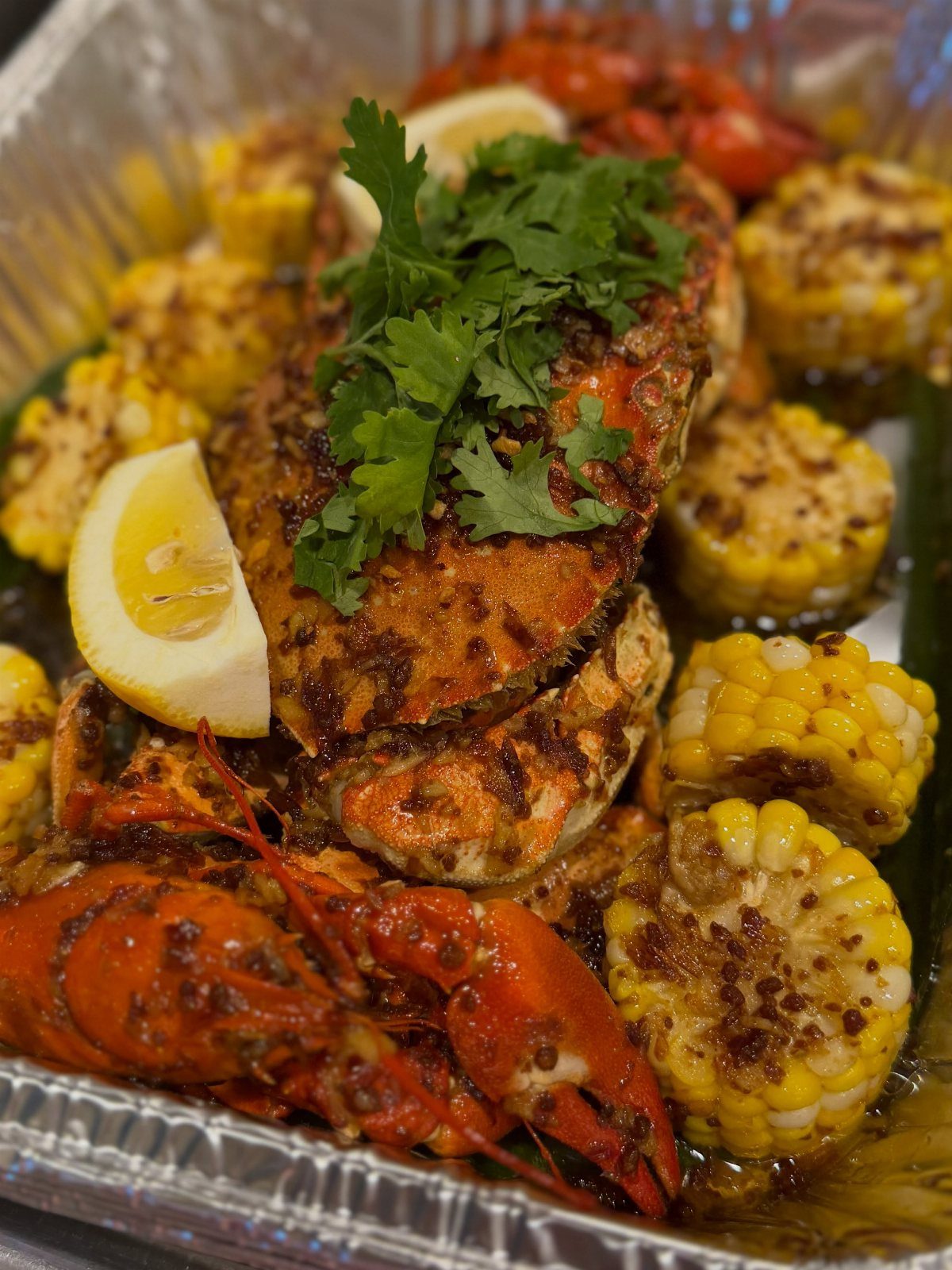 Seasoned crawfish, crab, and corn on the cob in a foil tray.