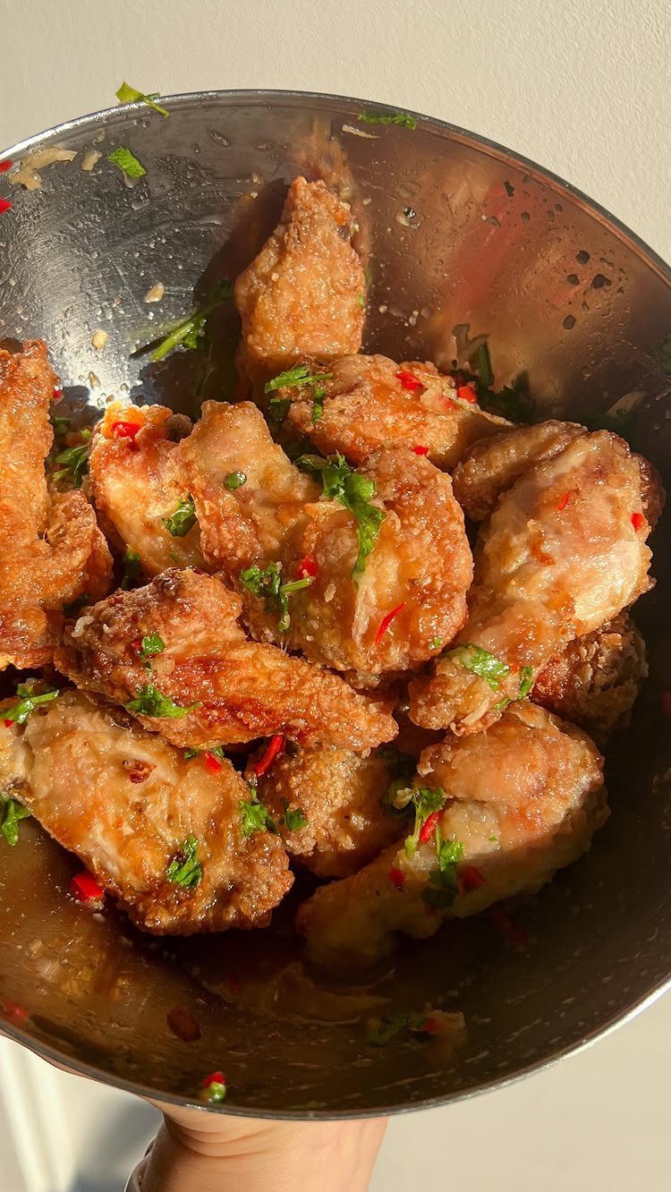 Fried chicken wings with red chilies and herbs in a metal bowl.