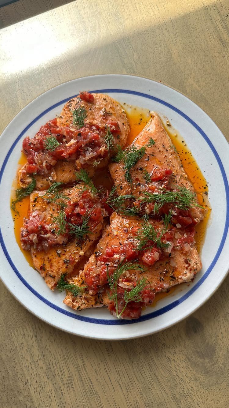 Roasted salmon fillets topped with tomato salsa and fresh dill on a white plate.