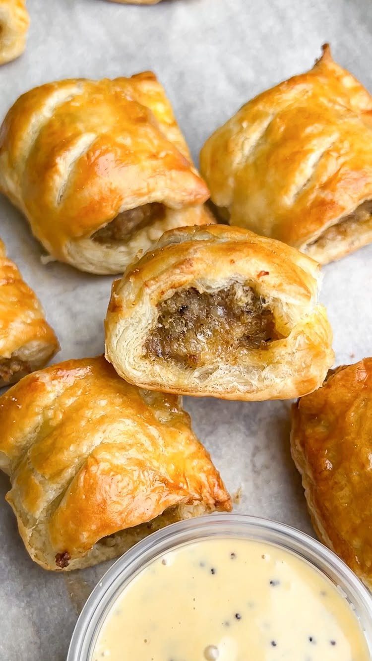 Golden-brown sausage rolls on parchment paper with a side of mustard dipping sauce.