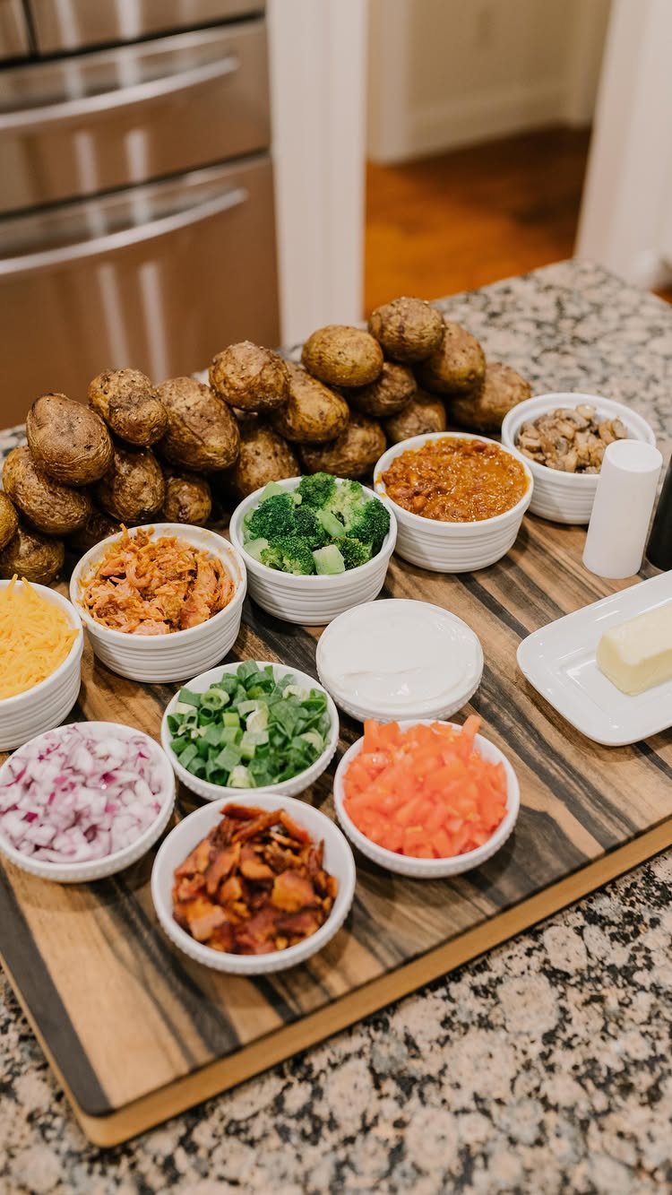 Baked potato bar with various toppings in white bowls on a wooden board.