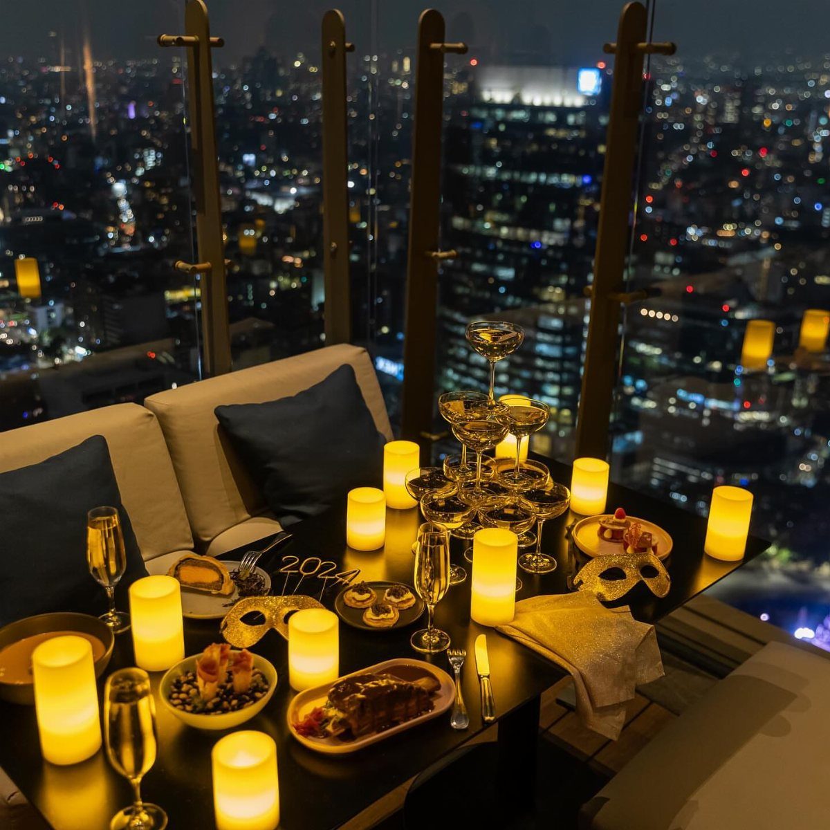 Rooftop table with champagne tower and glowing candles overlooking a city skyline at night
