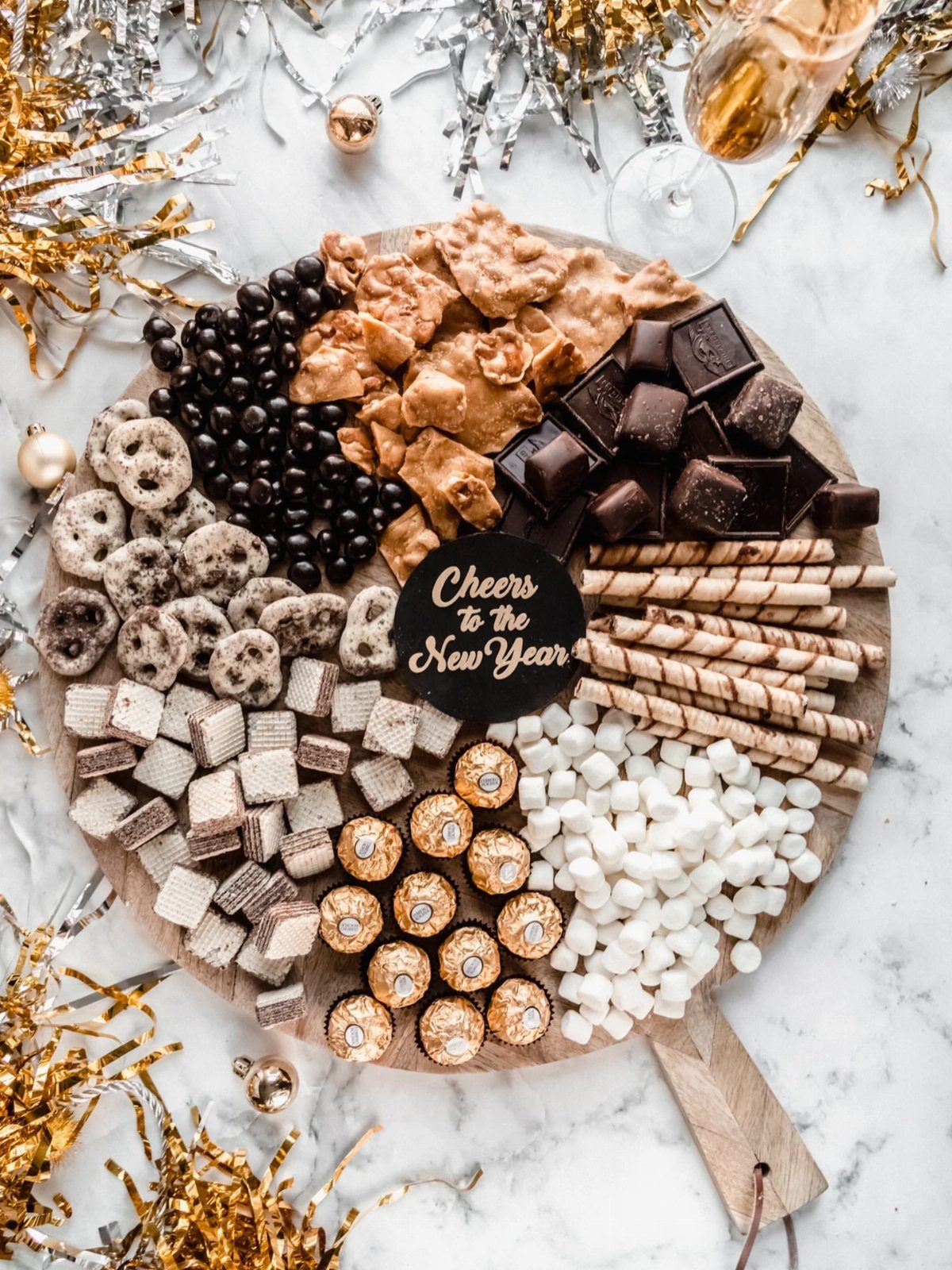 Dessert platter with chocolates and marshmallows surrounded by gold and silver New Year tinsel.