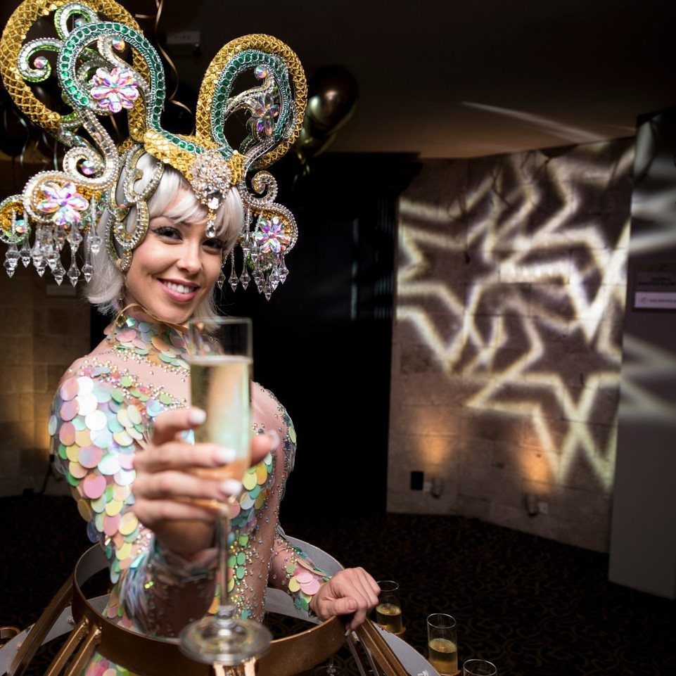 Woman in ornate jeweled headpiece and sequined dress holding a champagne glass.