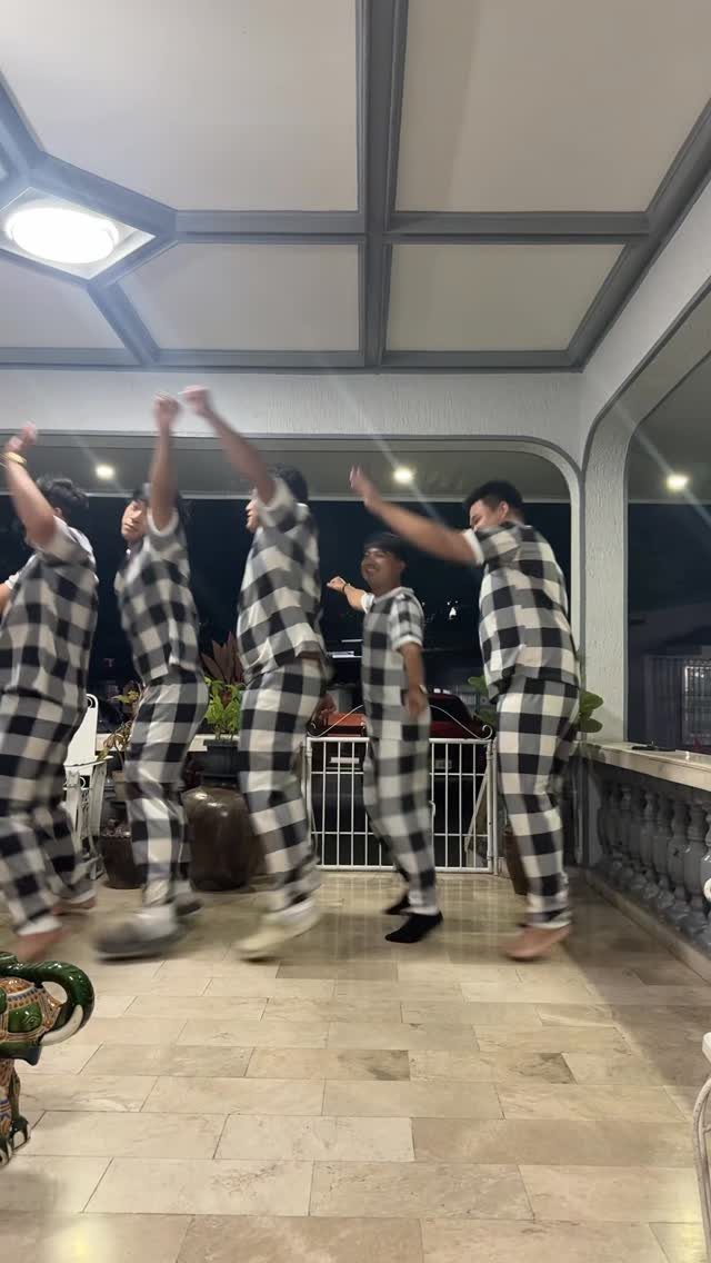Five people in matching checkered pajamas jumping and dancing on a tiled patio.