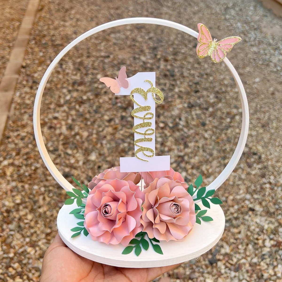 White circular centerpiece with pink paper roses and a gold glitter number one.