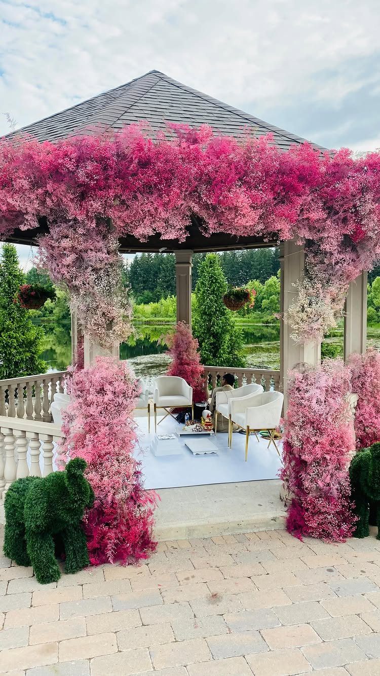 Gazebo decorated with pink flowers and white furniture on an outdoor stone patio