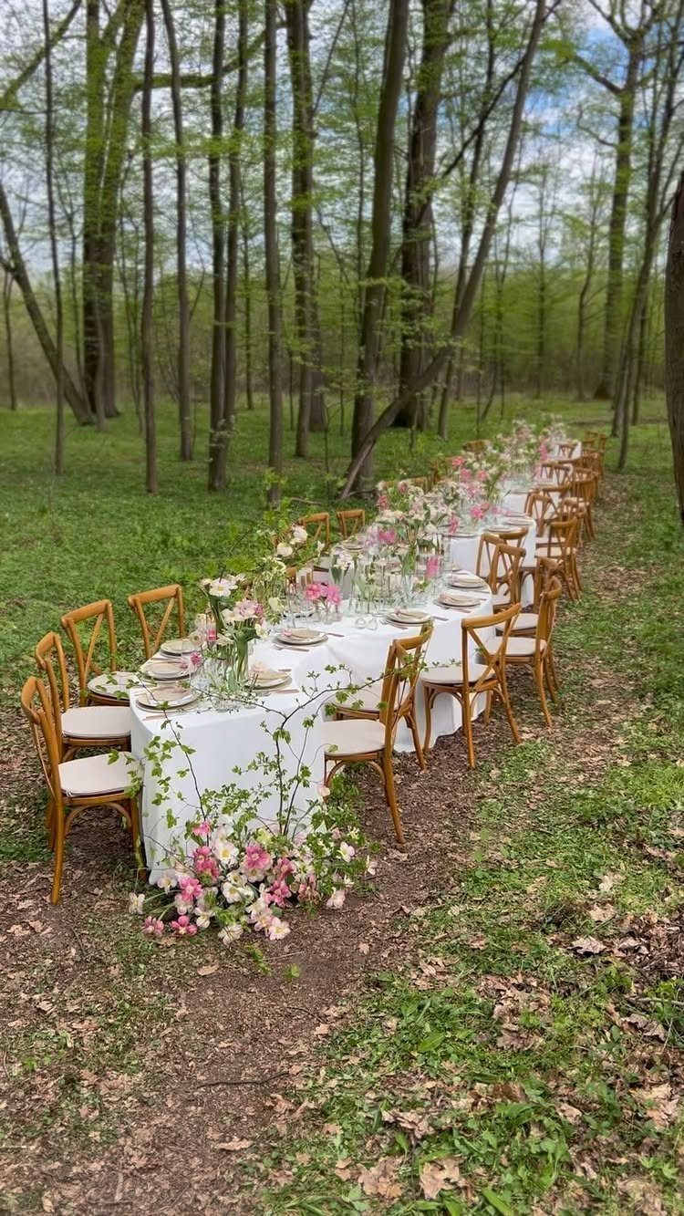 Long white dining table with pink and white floral arrangements in a forest
