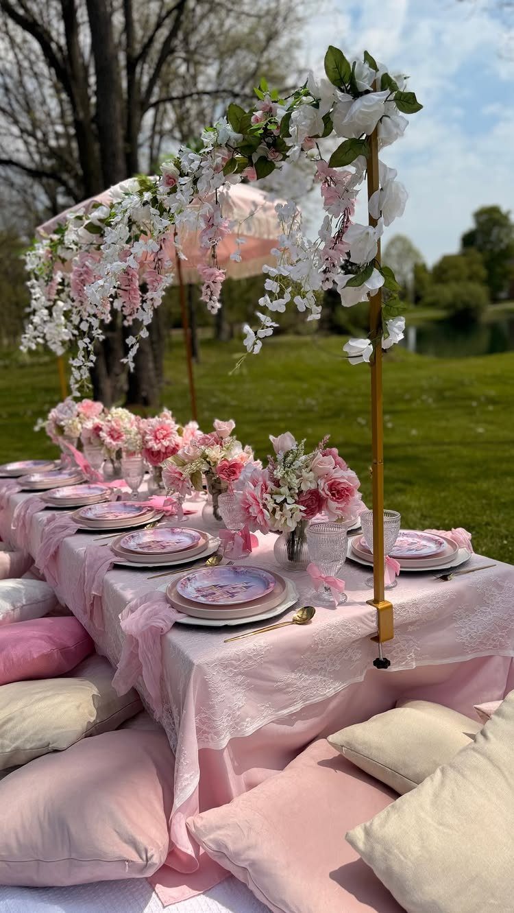 Low outdoor table with pink lace cloth, floral arrangements, and floor pillows.