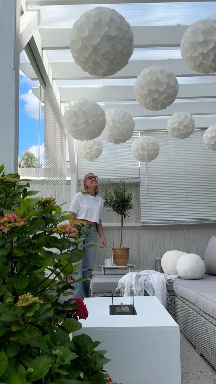White honeycomb paper lanterns hanging from a white outdoor patio pergola ceiling