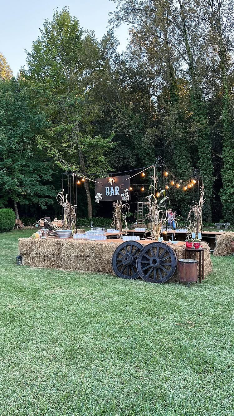 Outdoor party bar made of hay bales with wagon wheels and string lights.