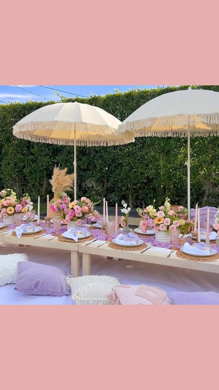 Outdoor picnic table with purple decor, floral centerpieces, and white fringed umbrellas.