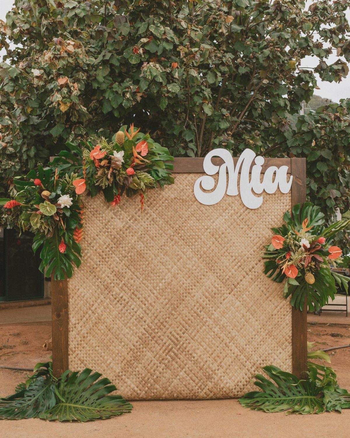 Woven straw photo backdrop with tropical flowers and a white Mia name sign.