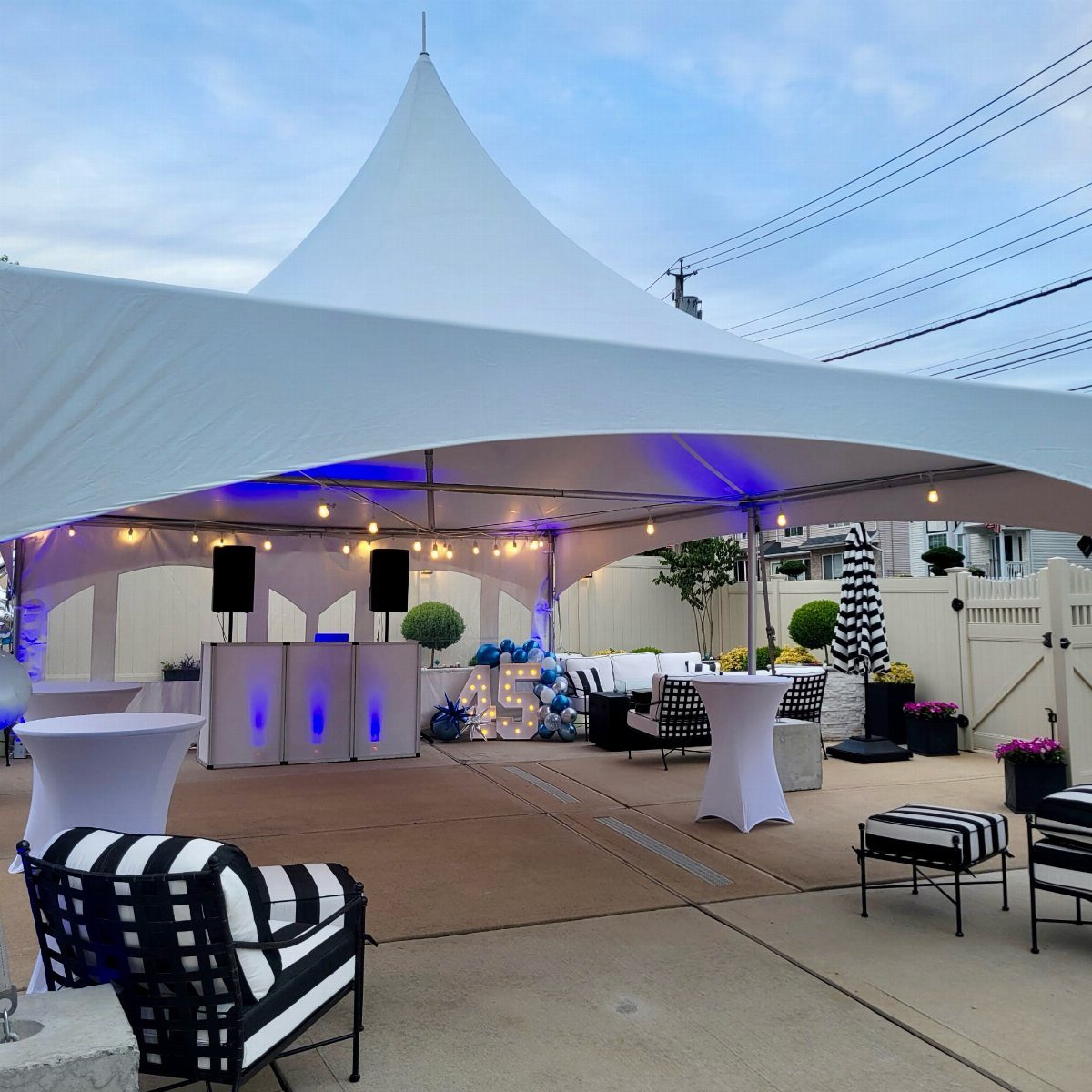 Large white peaked event tent with blue lighting and modern lounge furniture outdoors.