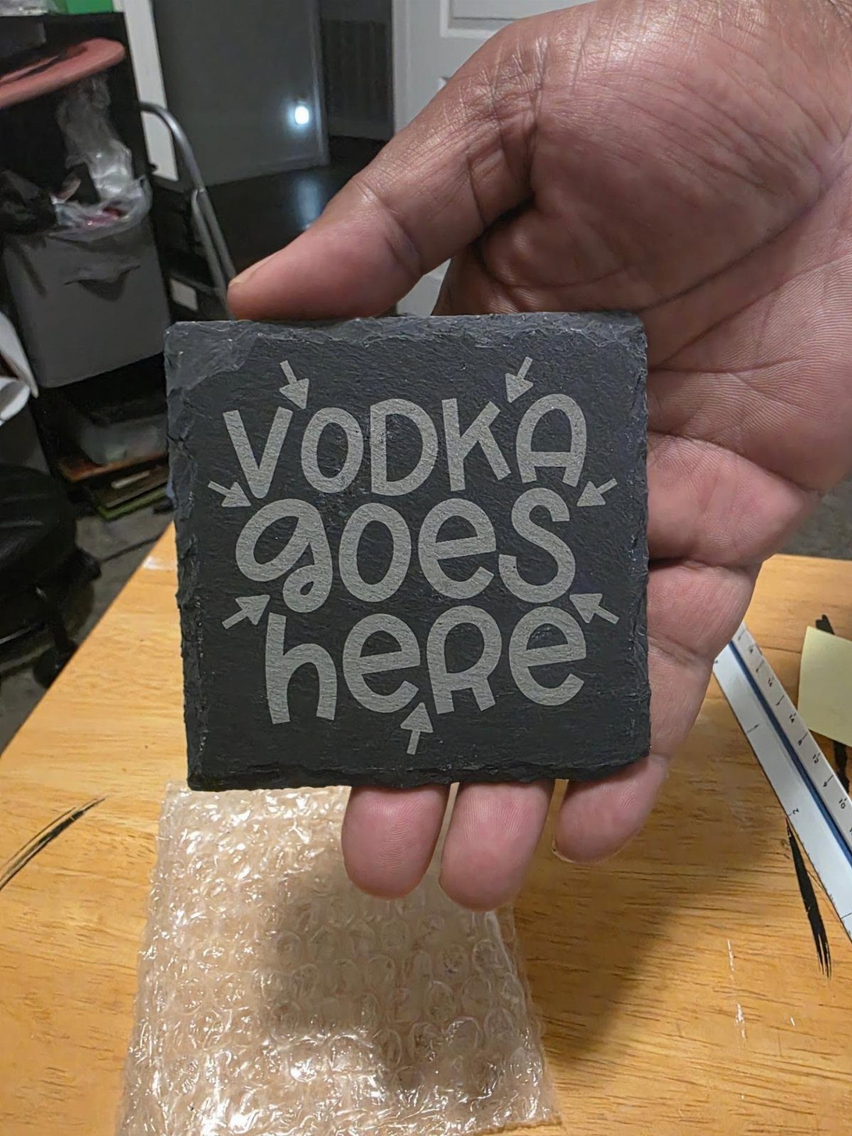 Slate coaster with engraved text saying vodka goes here held by a hand