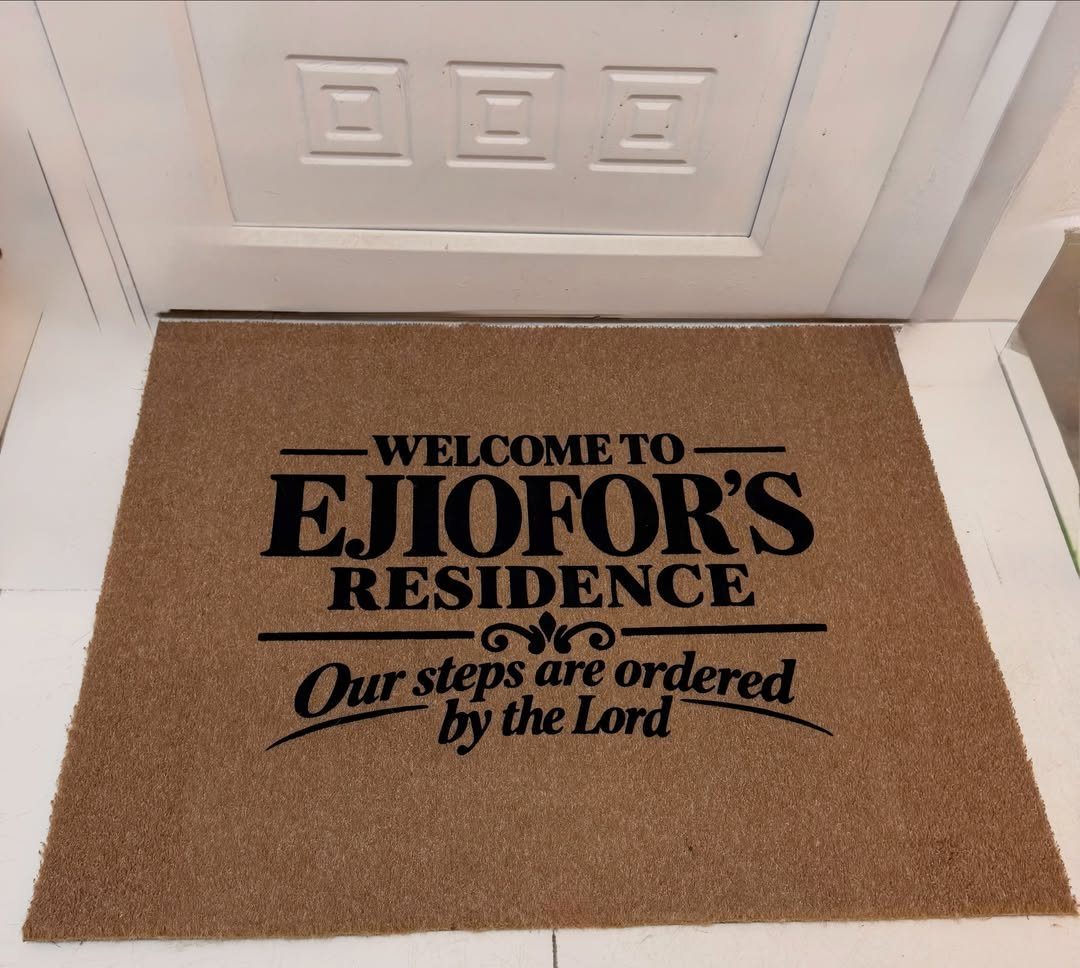 Brown coir doormat with personalized family name and religious quote before white door