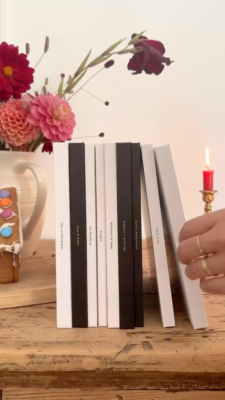 Hardcover photo books in white and black on a wooden table with flowers.