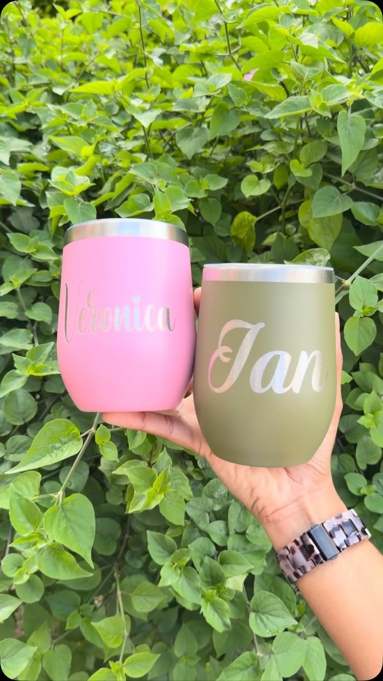 Two personalized insulated wine tumblers in pink and green held against green leaves.