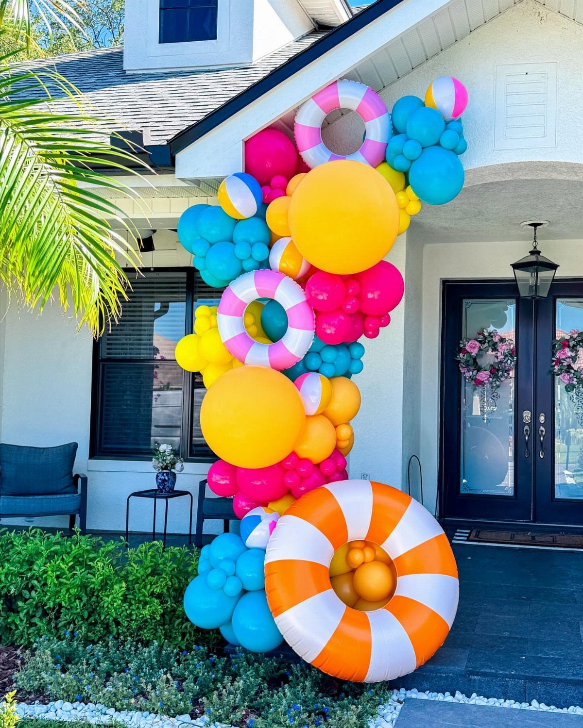 Colorful balloon installation with swim rings decorating the entrance of a white house.