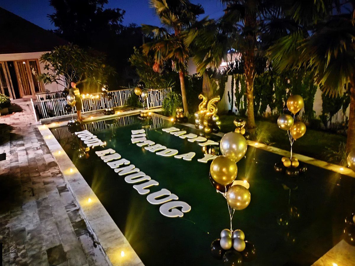 Floating white birthday letters and gold balloons in a swimming pool at night.