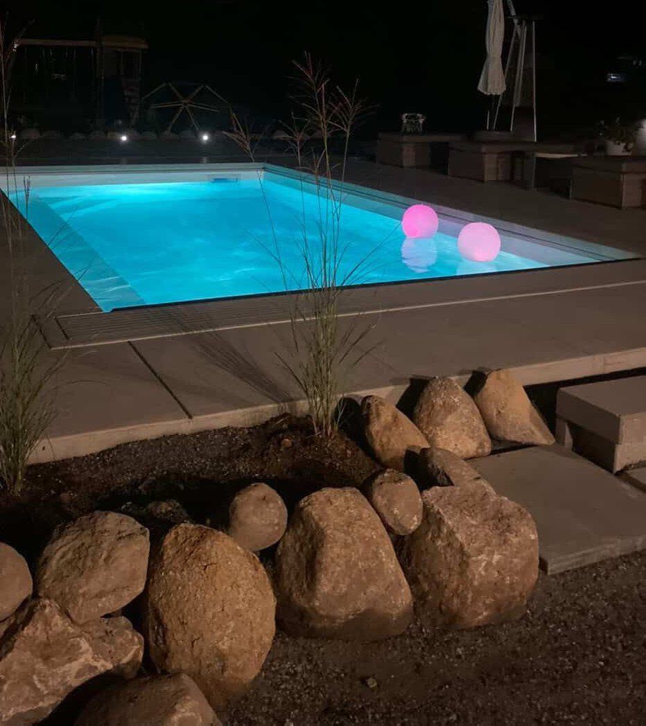 Glowing blue swimming pool at night with two pink floating neon spheres.