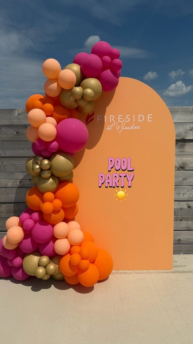 Orange arched backdrop with pool party text and colorful balloon garland outdoors.
