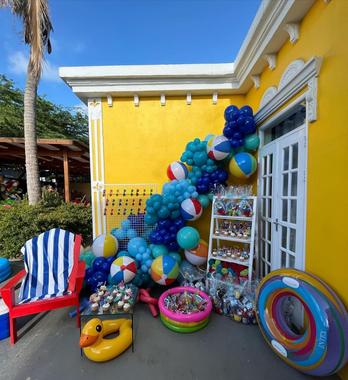 Festive snack station with cupcakes and treats surrounded by blue balloons and beach balls.