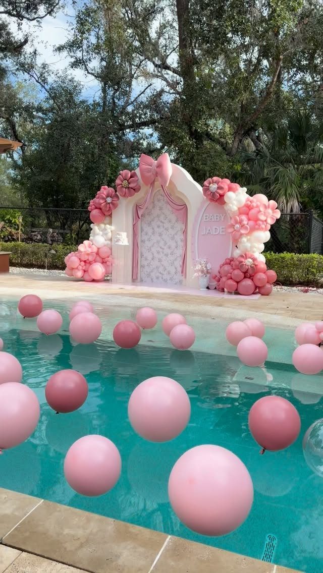 Pink balloons floating in a pool with a matching decorative party backdrop.