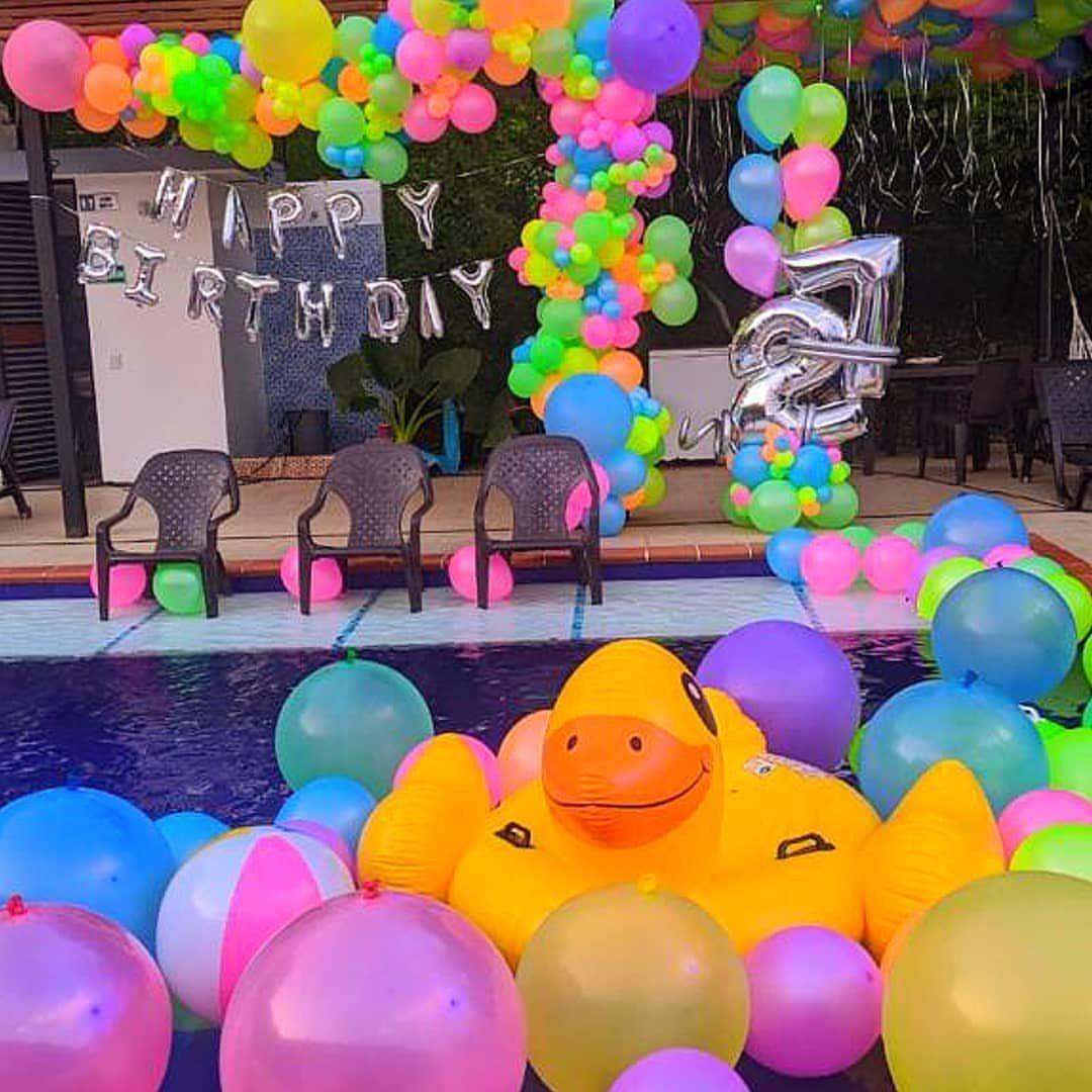 Colorful birthday decorations with balloons and a giant inflatable duck in a pool.