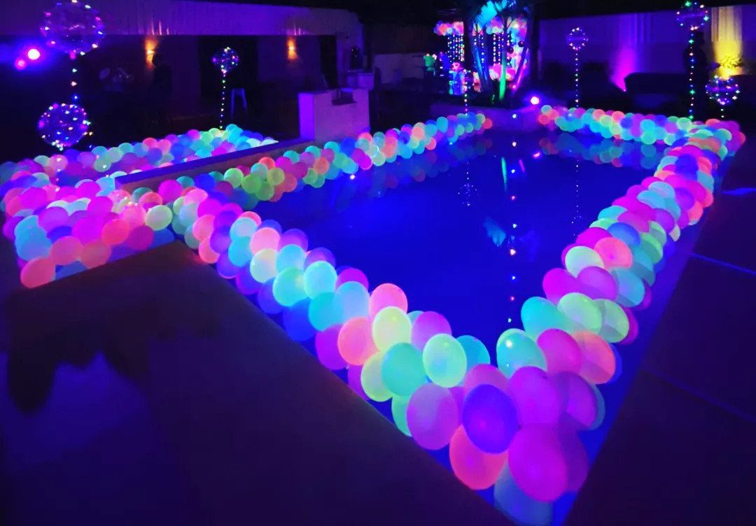 Glowing neon balloons in pink and blue lining the edge of a swimming pool