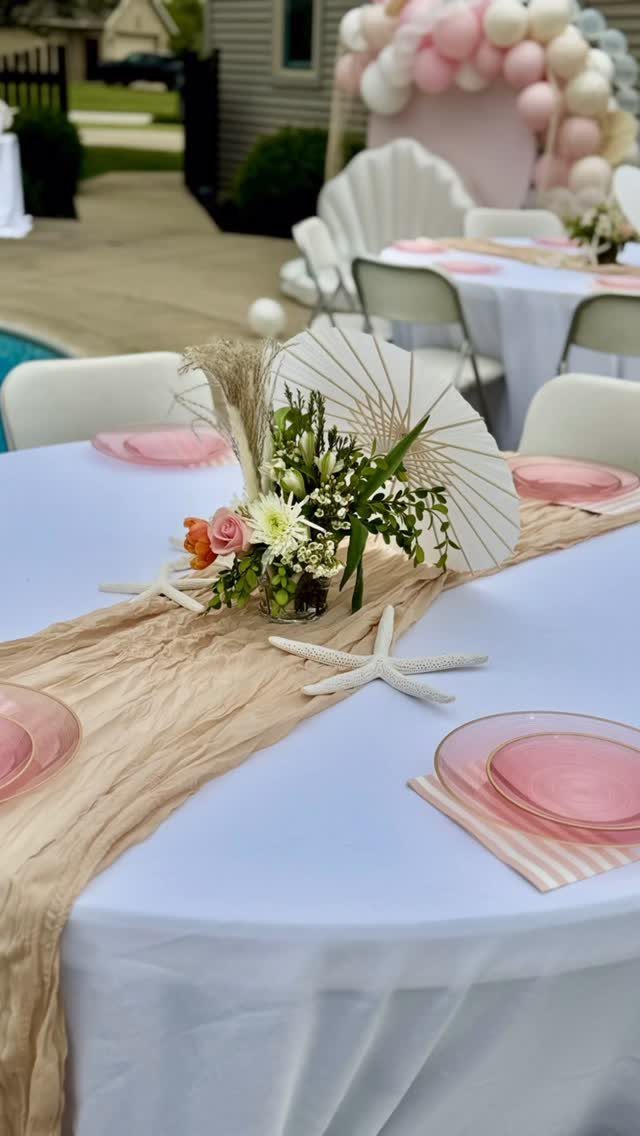 Table setting with pink plates, white starfish, and floral centerpiece for a party.