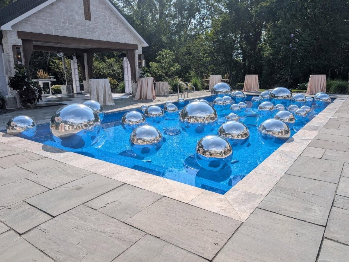 Silver metallic spheres floating in a blue swimming pool on a stone patio.