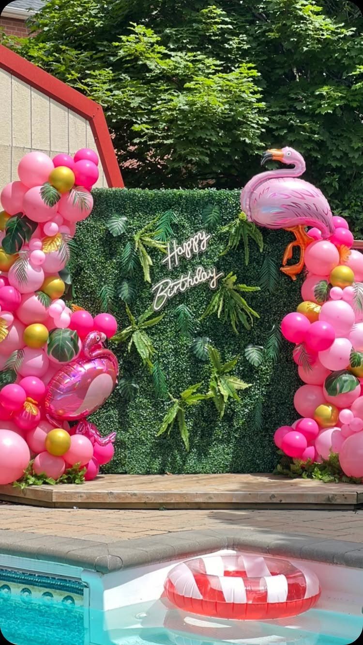 Pink flamingo inflatables and balloon arches framing a Happy Birthday neon sign wall.