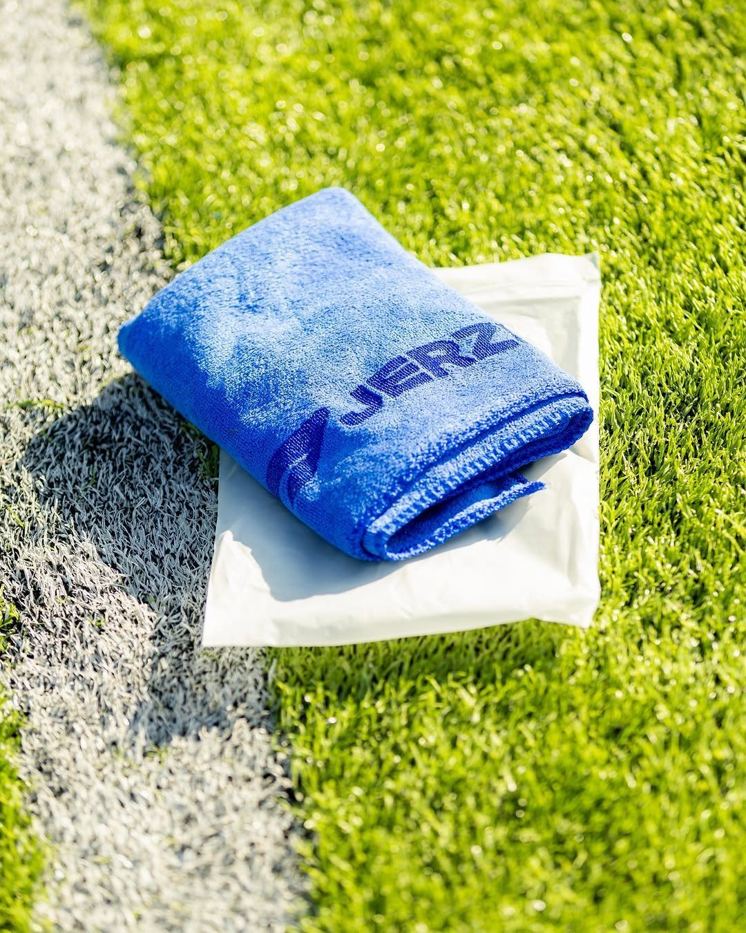 Blue microfiber cooling towel with branding resting on grass by a white line.