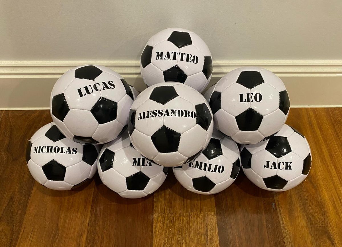 Small black and white soccer balls with personalized names on a wooden floor.