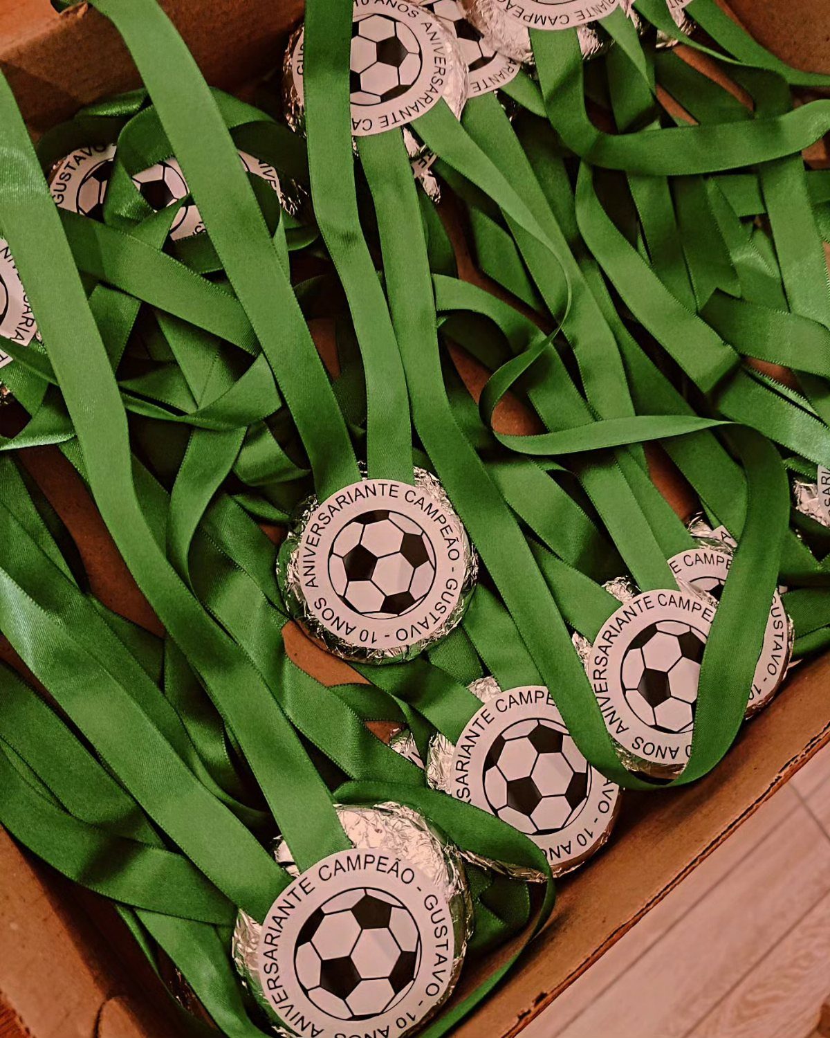Silver soccer medals with green ribbons piled inside a brown cardboard box.