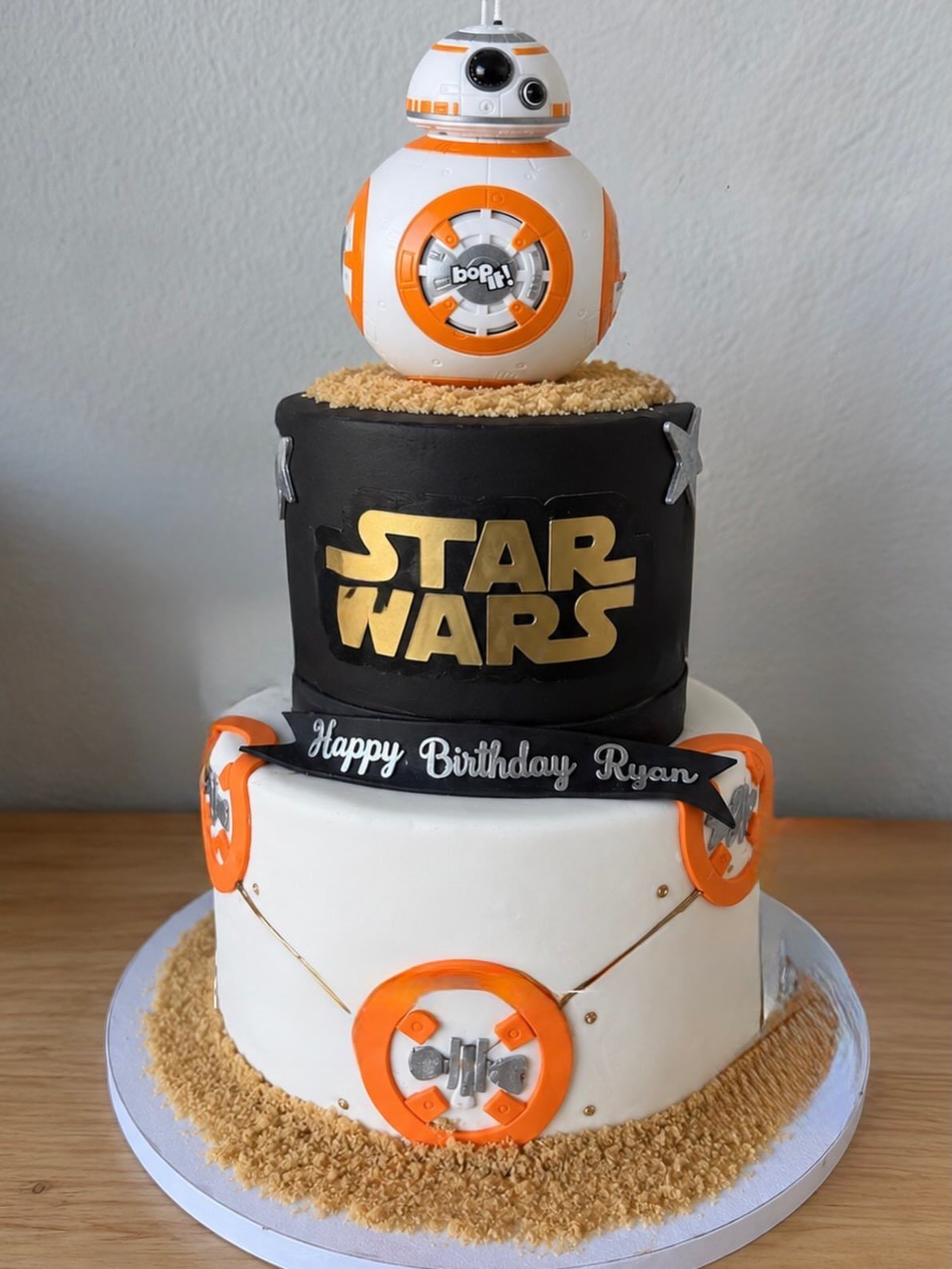 Three-tier Star Wars birthday cake topped with a BB-8 droid figure and gold logo.