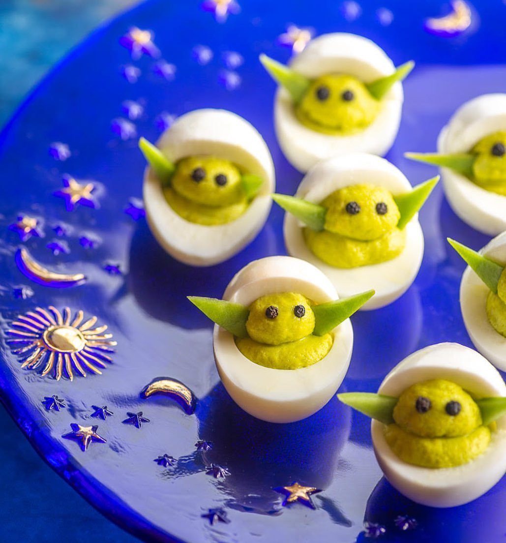 Deviled eggs styled as Grogu on a blue plate with gold stars.