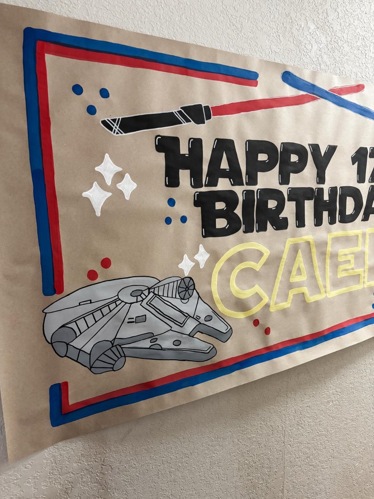 Hand-drawn Star Wars themed birthday banner with Millennium Falcon and lightsabers on brown paper.
