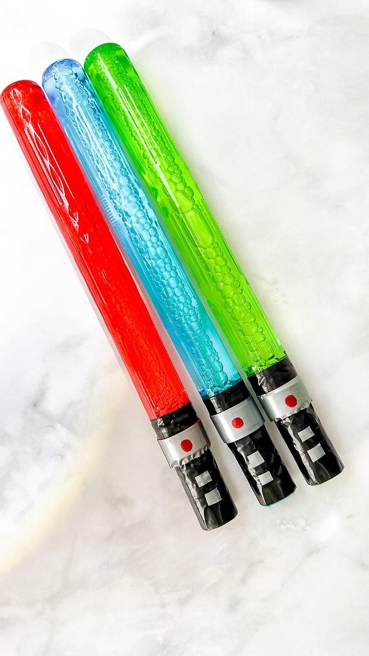 Three lightsaber-shaped gelatin treats in red, blue, and green on marble surface