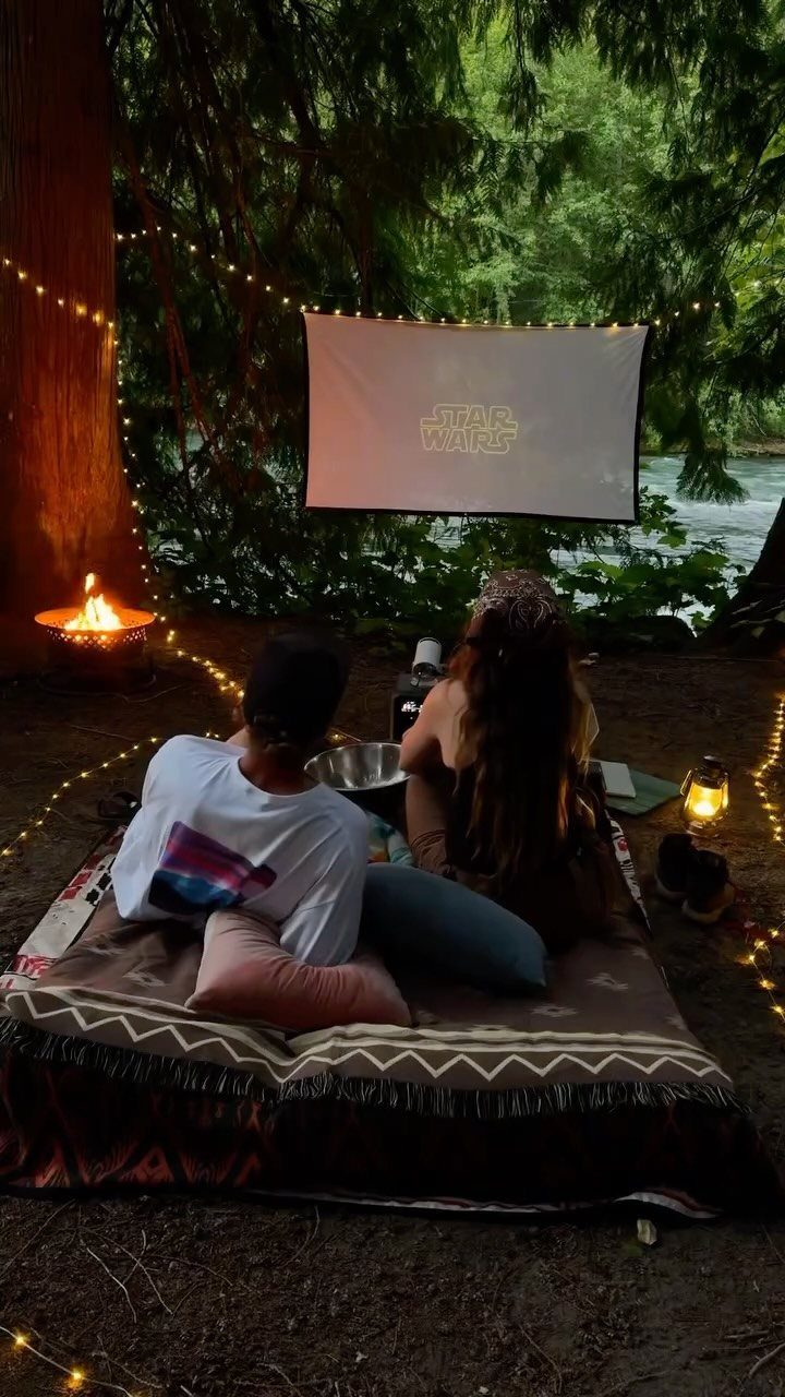 Two people watching a Star Wars movie on a projector screen in the woods