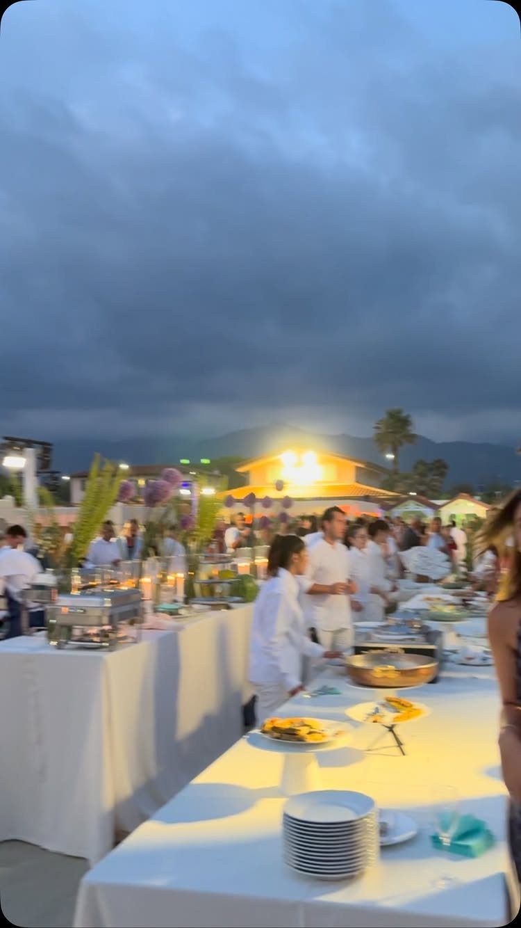 Outdoor evening party with white buffet tables and guests dressed in white clothing.