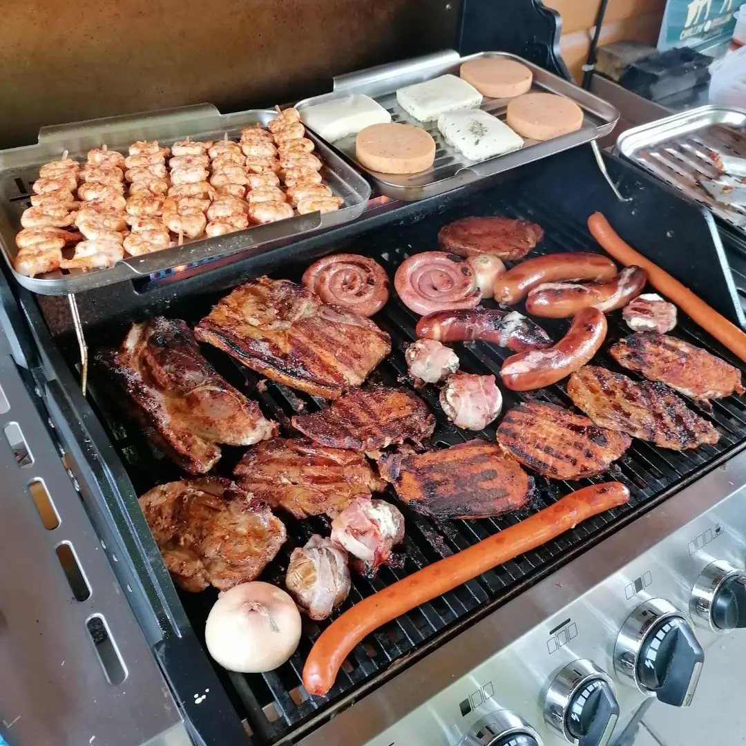 Assorted grilled meats, sausages, and skewers cooking on an outdoor barbecue grill