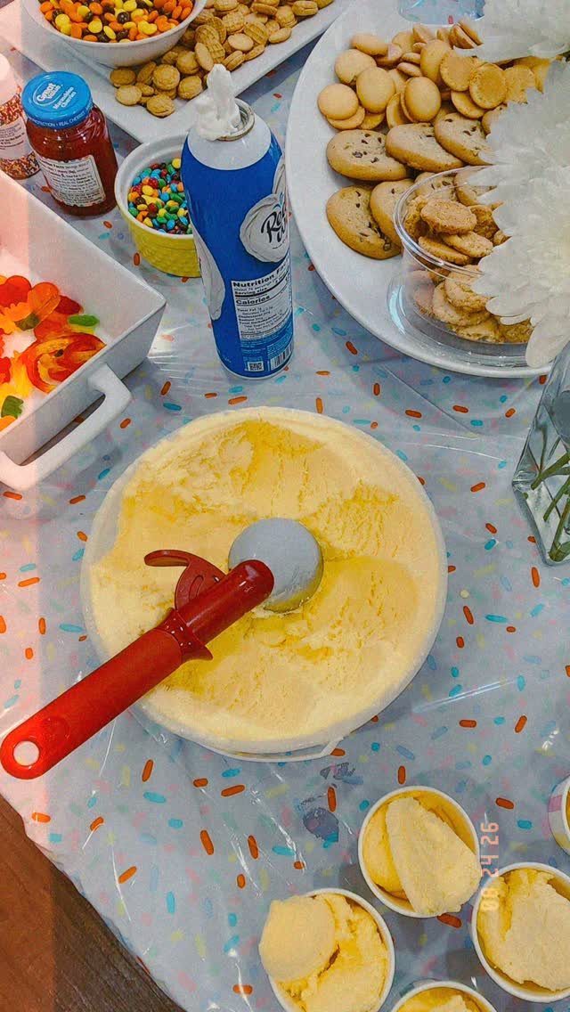 Yellow ice cream with a red scooper surrounded by various sweet toppings and cookies.